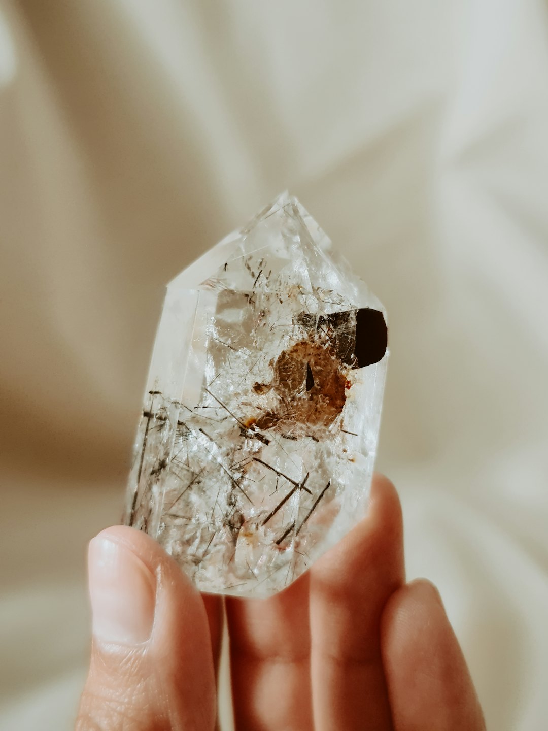 Una mano sostiene un cristal de cuarzo transparente con inclusiones minerales oscuras.