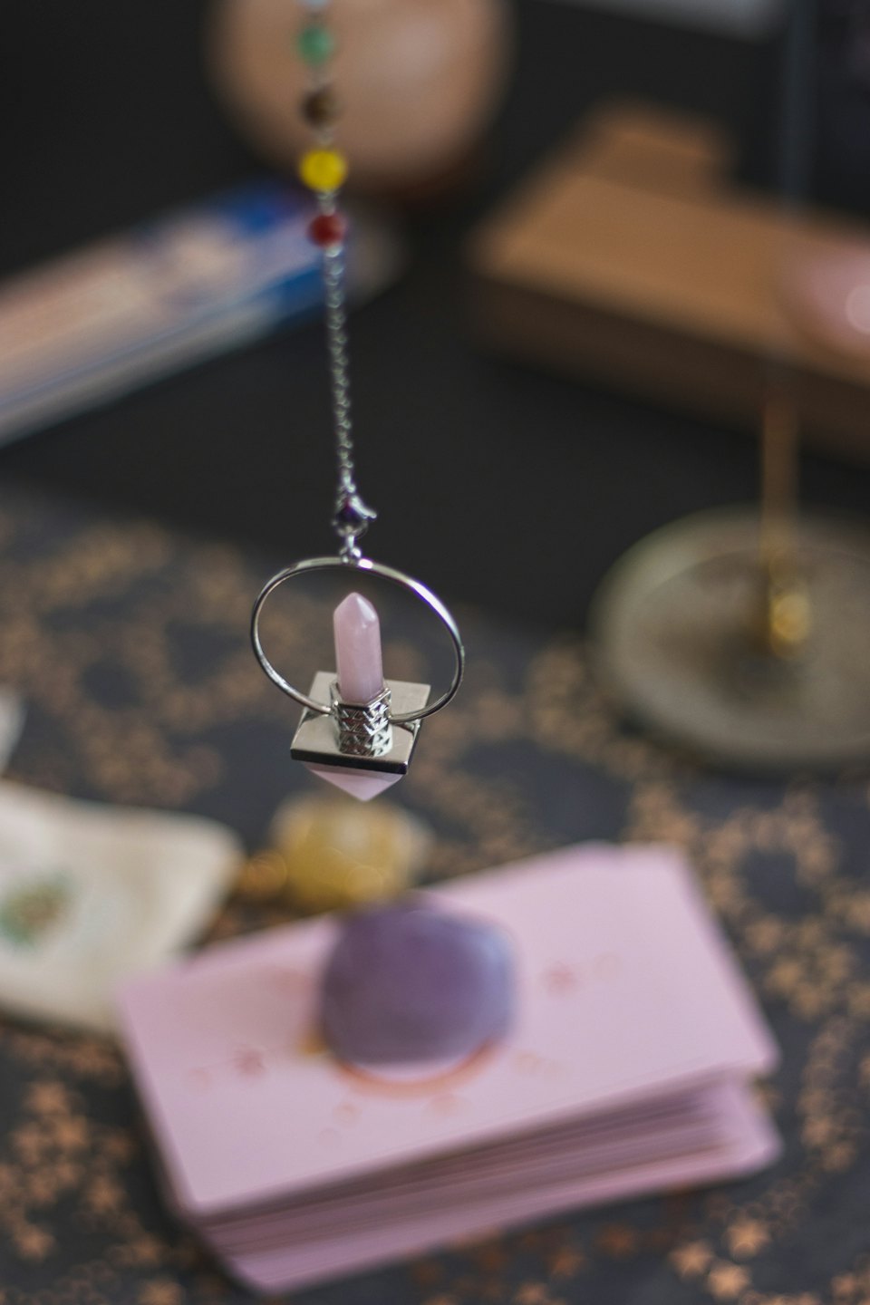 Un péndulo de cuarzo rosa cuelga sobre cartas del tarot y cristales.